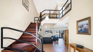 A wooden staircase with black railings leading to an upper floor. A black leather sofa and a wooden console table are visible in the living area below. - Great value 2 bedroom apartment in the heart of South Fremantle (Fremantle)