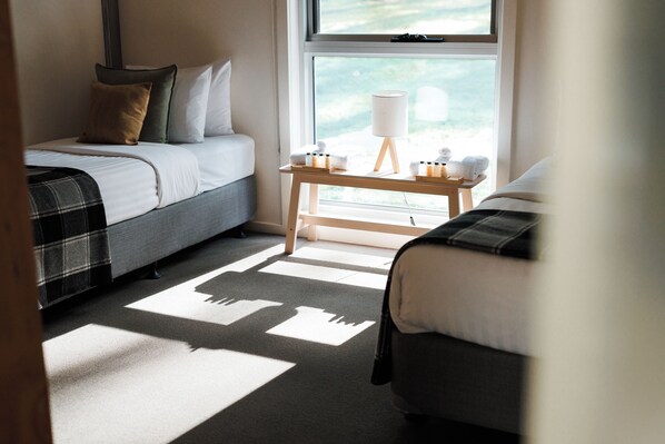 A bedroom with two beds, a bedside table with toiletries, and a window with a view.