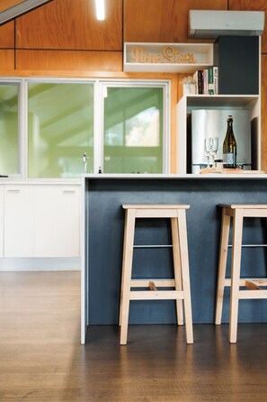 A modern kitchen with wooden cabinets, a bar area with stools, and a wine bottle.