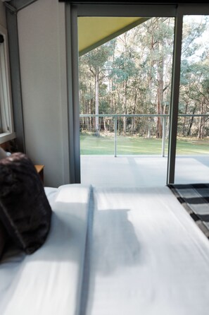 A bed with white sheets and a dark pillow in a room with a large window.