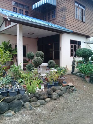 Une maison dotée d’un porche abrité, de plantes en pot et d’un jardin agrémenté de rochers et de différentes espèces végétales.