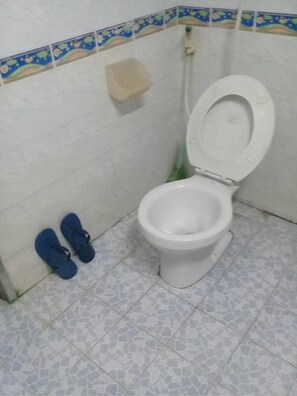 Un baño con inodoro blanco, un par de pantuflas azules y piso de baldosas.