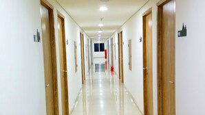 Un largo pasillo bien iluminado con puertas de madera a ambos lados, que conduce a una habitación luminosa al final.