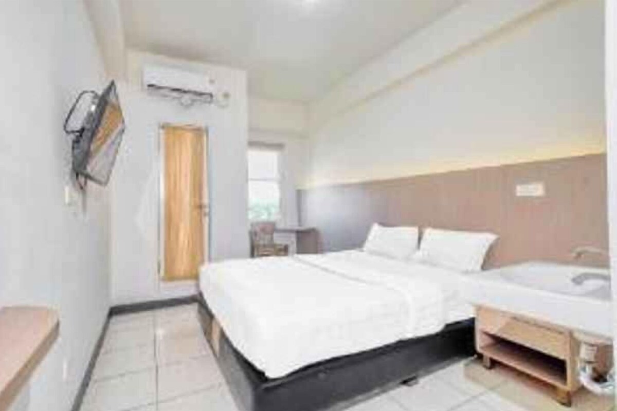 A hotel room with a bed, bedside table, and a small desk with a chair.