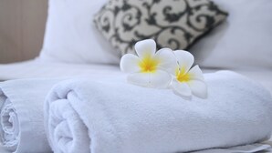 Una cama bien hecha con toallas blancas y dos flores blancas.