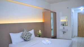 Una habitación de hotel con cama, mesita de noche, espejo, lavabo y puerta.