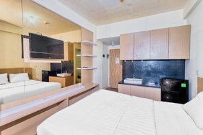 A modern hotel room with a large bed, a flat-screen TV mounted on a wall, a small kitchenette, and a mirror reflecting the room.