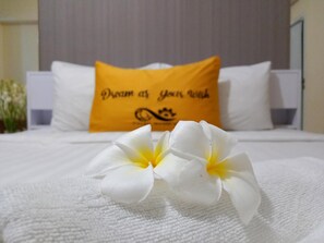 A bed with white bedding and a yellow pillow with text.