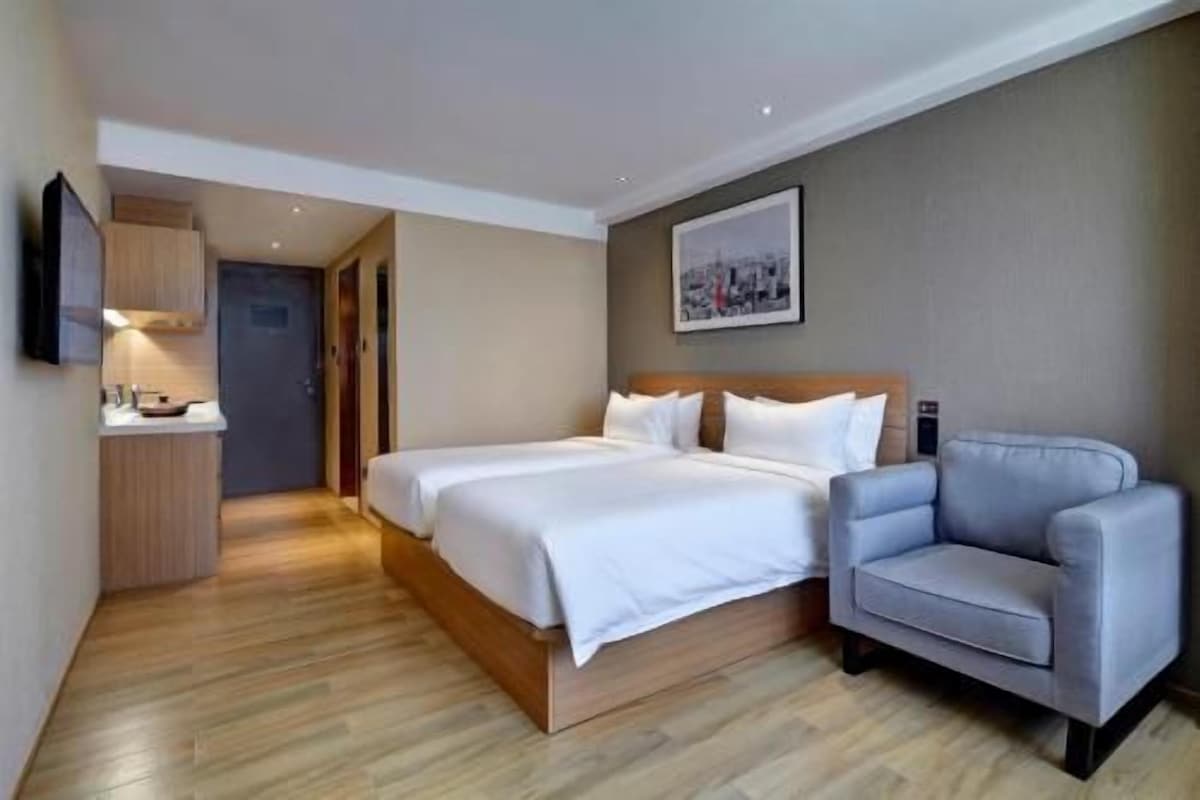 Habitación de hotel con cama doble, un sillón gris, un armario de madera y un televisor de pantalla plana.