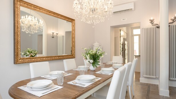 A dining room with a large mirror, chandelier, and white chairs.