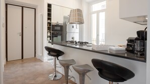 A modern kitchen with a central island, bar stools, and a hanging light fixture.