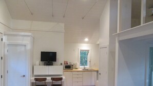 Un espacio habitable compacto con kitchenette, una zona de comedor con dos sillas, un televisor y una ventana con vistas a árboles.
