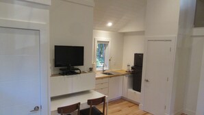Cocina compacta con televisor, lavabo y refrigerador. Hay dos sillas de madera y una mesa pequeña.