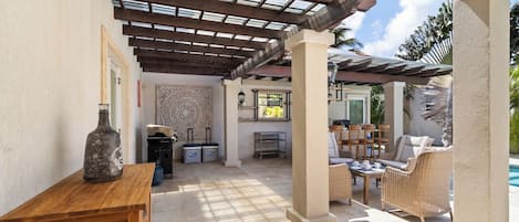 Un patio exterior con pérgola, mobiliario, piscina y zona de bar.