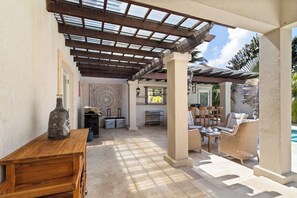 Een buitenterras met een pergola, zitplaatsen, een zwembad en een bar.