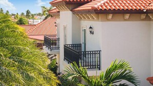 A building with a red-tiled roof, a balcony with black railings, and a door with a light fixture. - Upscale 5BR Villa: Game Room, Private Pool, Patio (Noord)