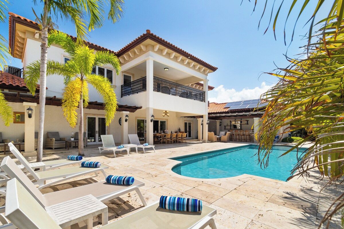 A two-story building with a swimming pool, outdoor seating, and palm trees.