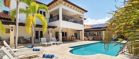 Un edificio de dos pisos con piscina, mobiliario exterior y palmeras.