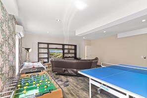 Ein Raum mit Kicker, Tischtennisplatte, einer Couch und einem Fernseher.
