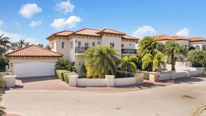A multi-story residential building with a red-tiled roof, a garage, and a landscaped front yard with palm trees. - Upscale 5BR Villa: Game Room, Private Pool, Patio (Noord)