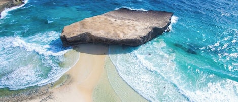 A beach with clear turquoise waters and a large rock formation.