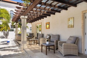 Un área de estar exterior con mobiliario de mimbre, una pérgola y vistas a un edificio.