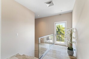 Una escalera con barandilla de cristal que lleva a un balcón con vistas a zonas verdes.
