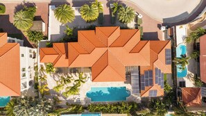 Luftaufnahme eines Resorts mit mehreren Gebäuden, einem Swimmingpool und Palmen.
