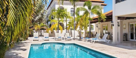 A swimming pool with lounge chairs, palm trees, and a building with a tiled roof.