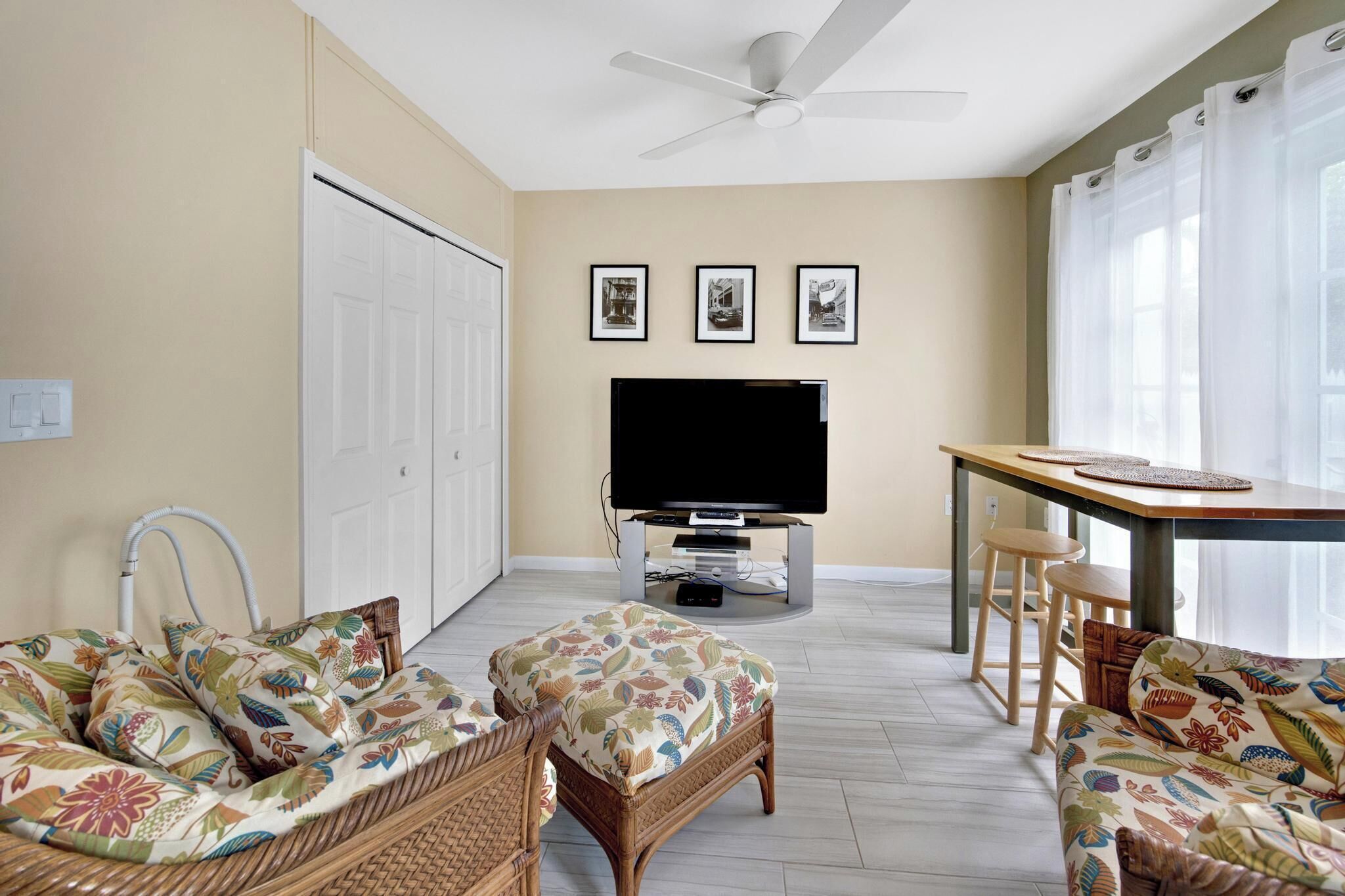 A living room with a television, wicker furniture, and a ceiling fan.
