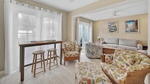 A living room with a sofa, a chair, a dining table with stools, and a ceiling fan.