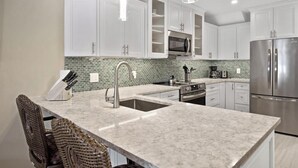 A modern kitchen with white cabinets, a stainless steel refrigerator, a microwave, and a sink.