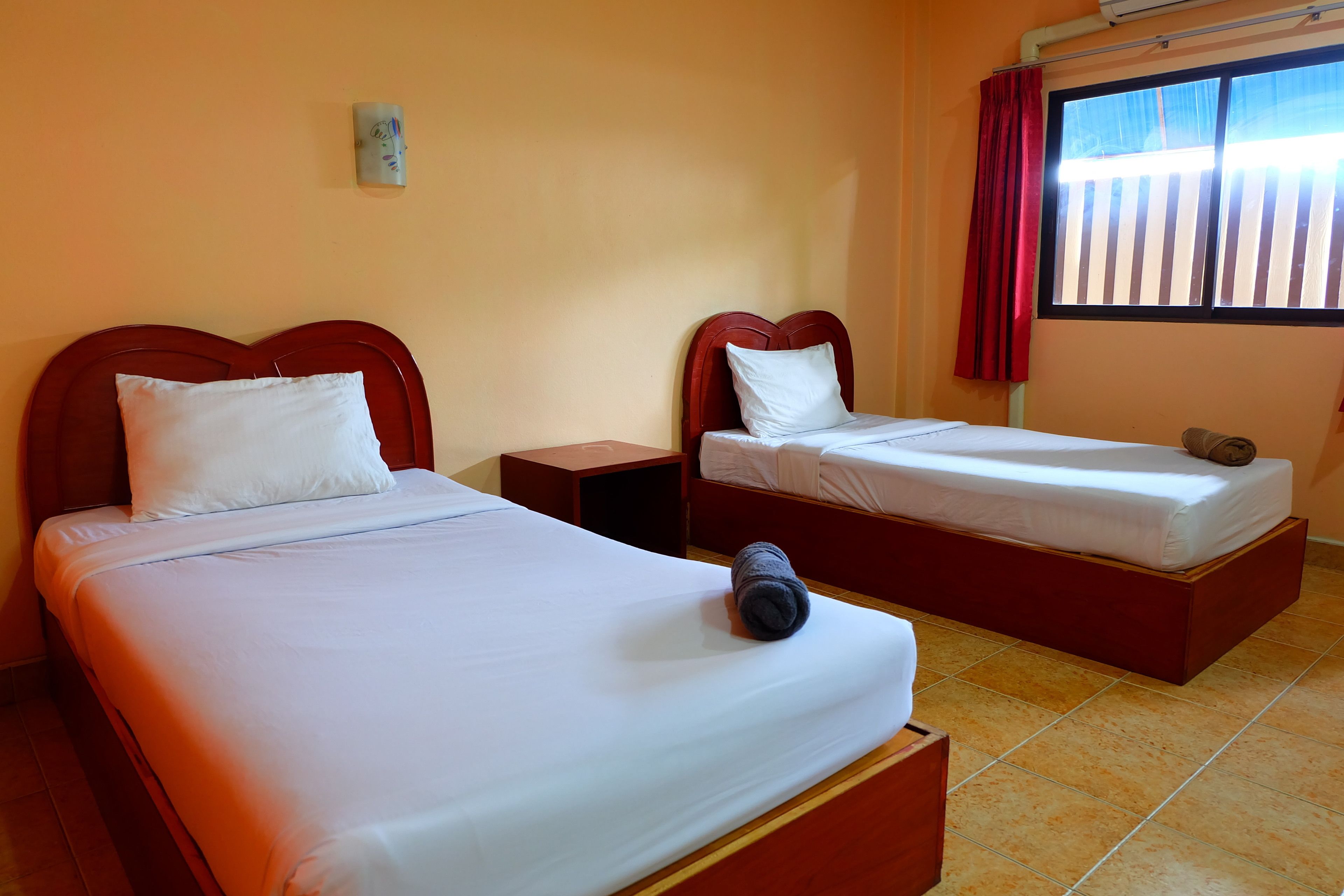 A hotel room with two single beds, a nightstand, a small table, and a window with curtains.