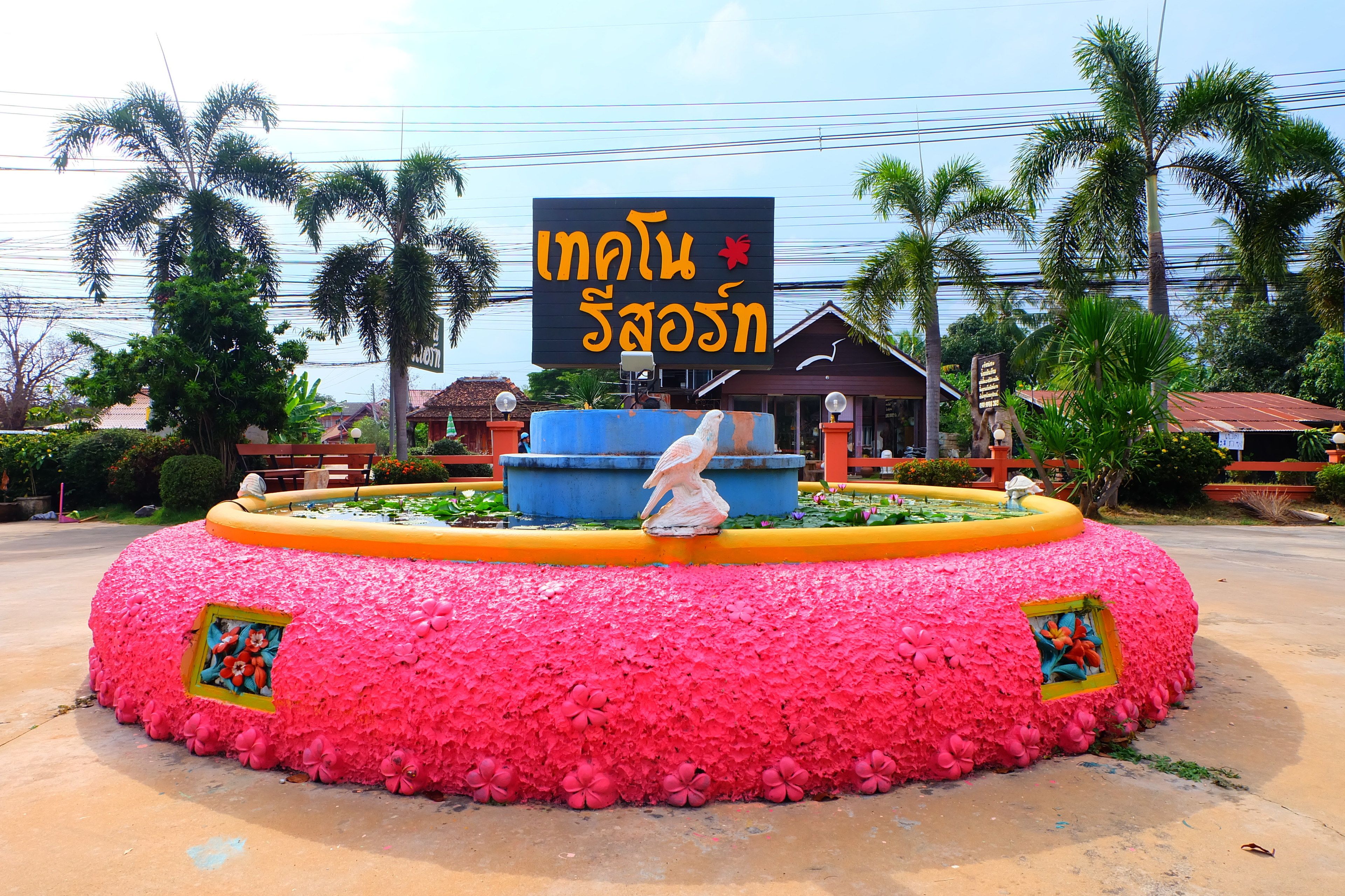 A circular flower bed with a statue in the center, surrounded by a sign with Thai text.
