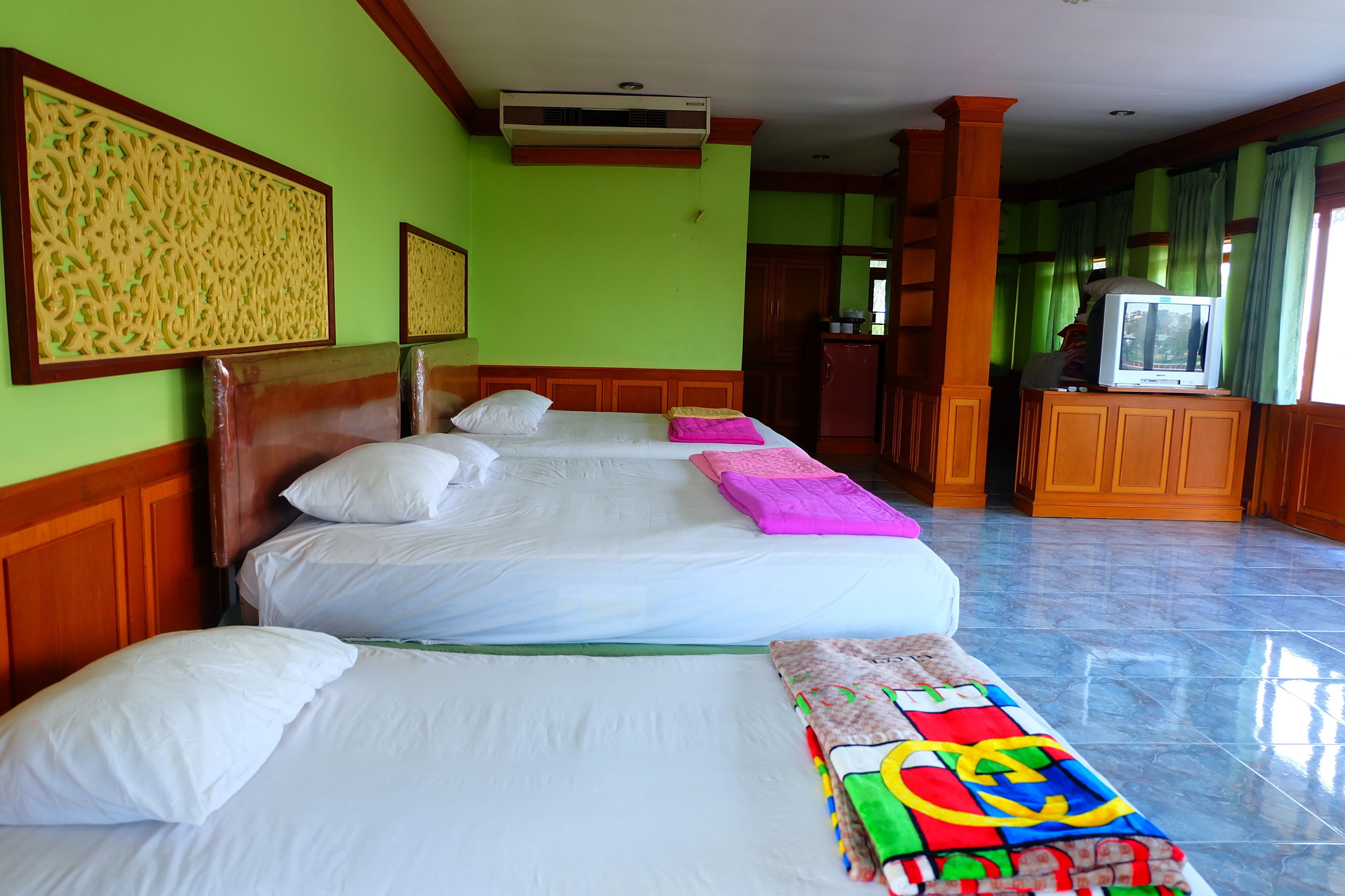 A hotel room with three beds, a television, and a kitchenette.