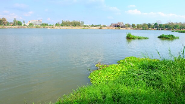 A calm lake with grassy banks and distant buildings. - Techno Riverview Resort (Kamphaeng Phet)