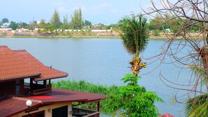 A building with a red roof and a balcony overlooking a body of water. - Techno Riverview Resort (Kamphaeng Phet)