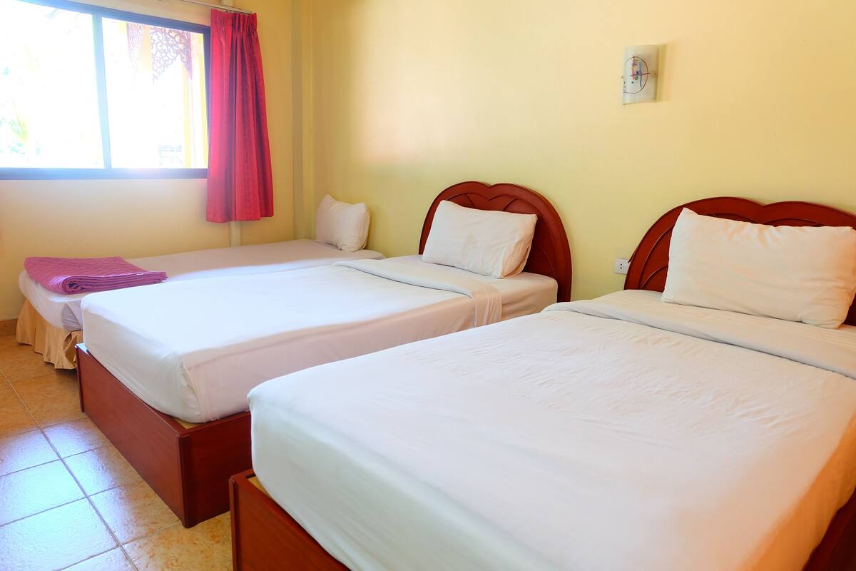 A room with two single beds, a window with a curtain, and a wall-mounted thermostat.