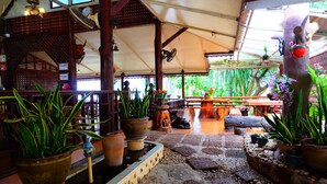 A covered outdoor area with stone flooring, potted plants, and wooden furniture. - Techno Riverview Resort (Kamphaeng Phet)