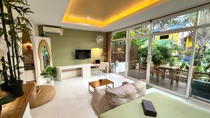 A modern living room with a sofa, coffee table, and TV, a balcony with outdoor furniture, and a large window with a view of greenery. - Beach Jungle Koh Chang (Ko Chang)