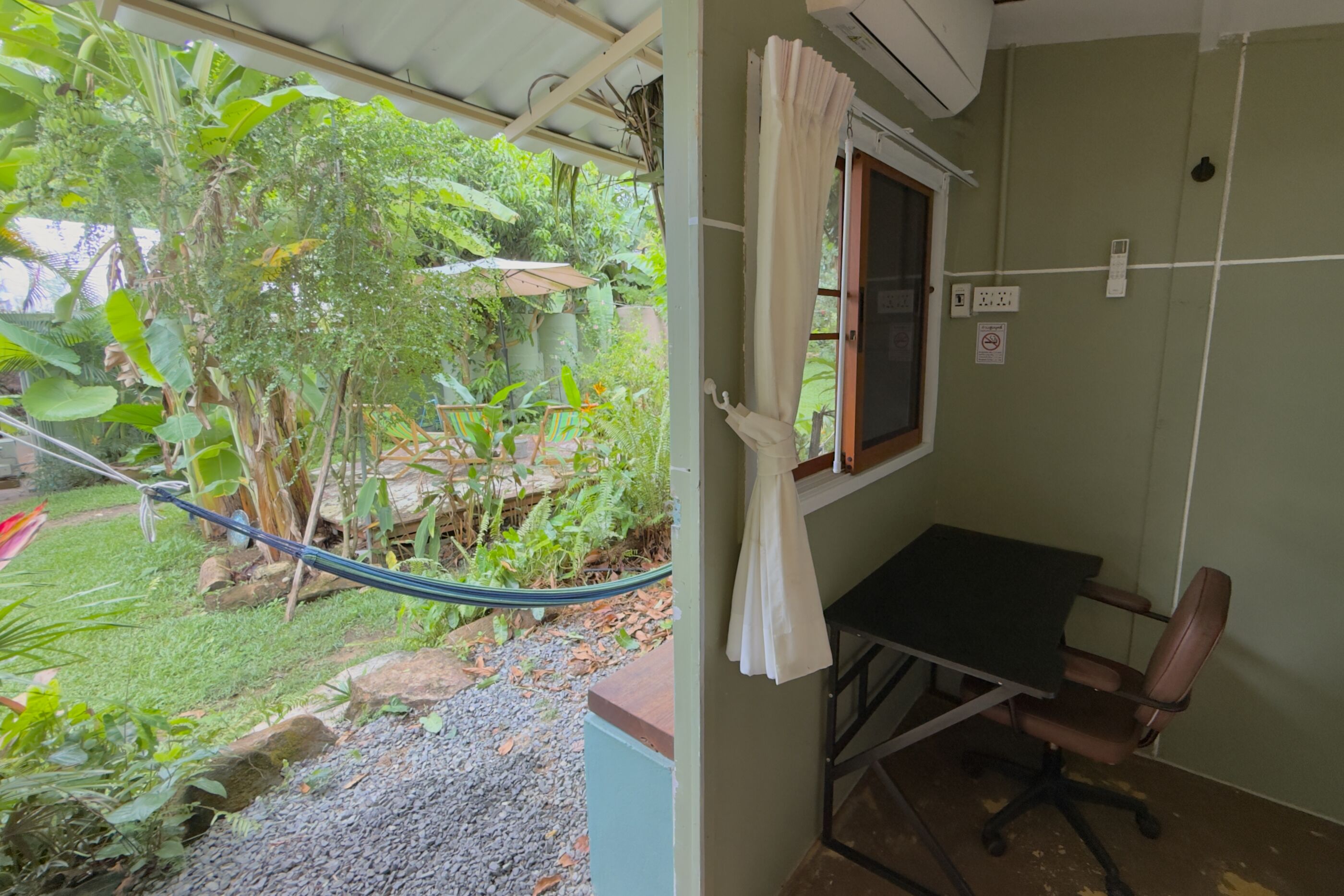 Una habitación con escritorio, silla y ventana con vistas a un jardín.