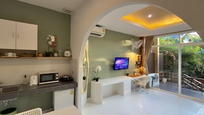 A modern kitchen with a microwave, sink, and cabinets, a dining area with a white table and chairs, and a large window with a view of greenery. - Beach Jungle Koh Chang (Ko Chang)