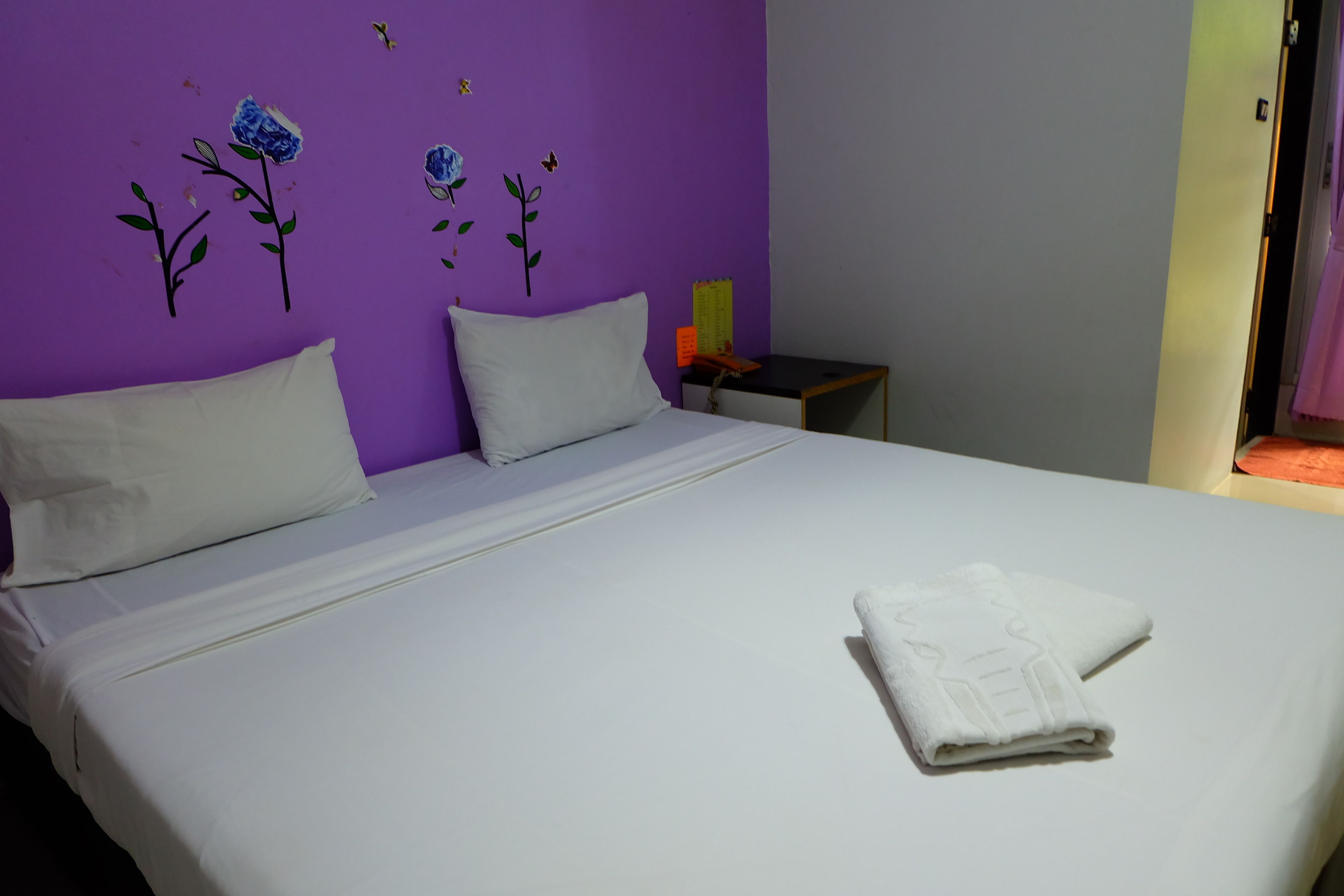 Uma cama bem arrumada com lençóis brancos e uma toalha dobrada sobre ela.