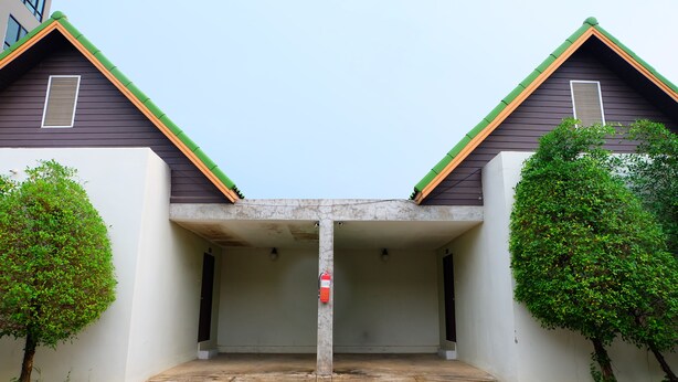 A building with a covered entrance, two trees, and a fire extinguisher. - Golden Place Guesthouse (Kamphaeng Phet)