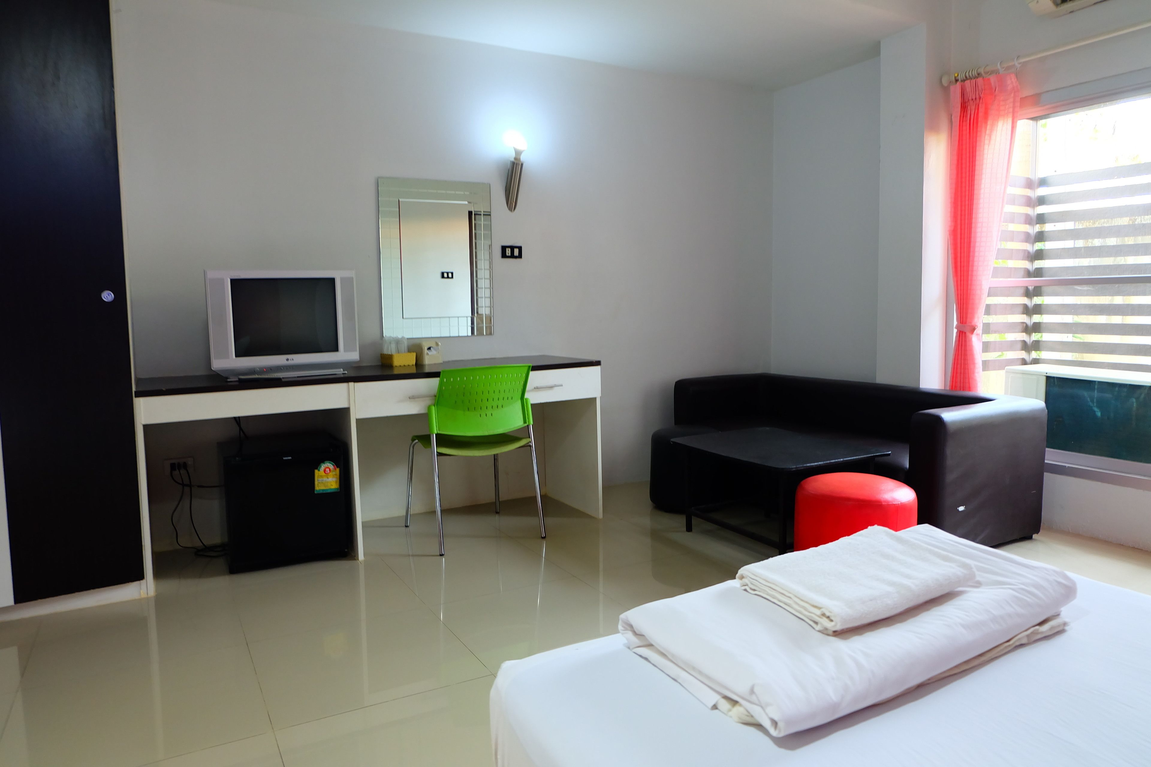A hotel room with a bed, a desk with a computer, a chair, a couch, and a window with curtains.