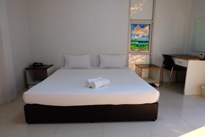 A modern hotel room with a large bed, a desk, and a window with a view of a field and sky. - Golden Place Guesthouse (Kamphaeng Phet)