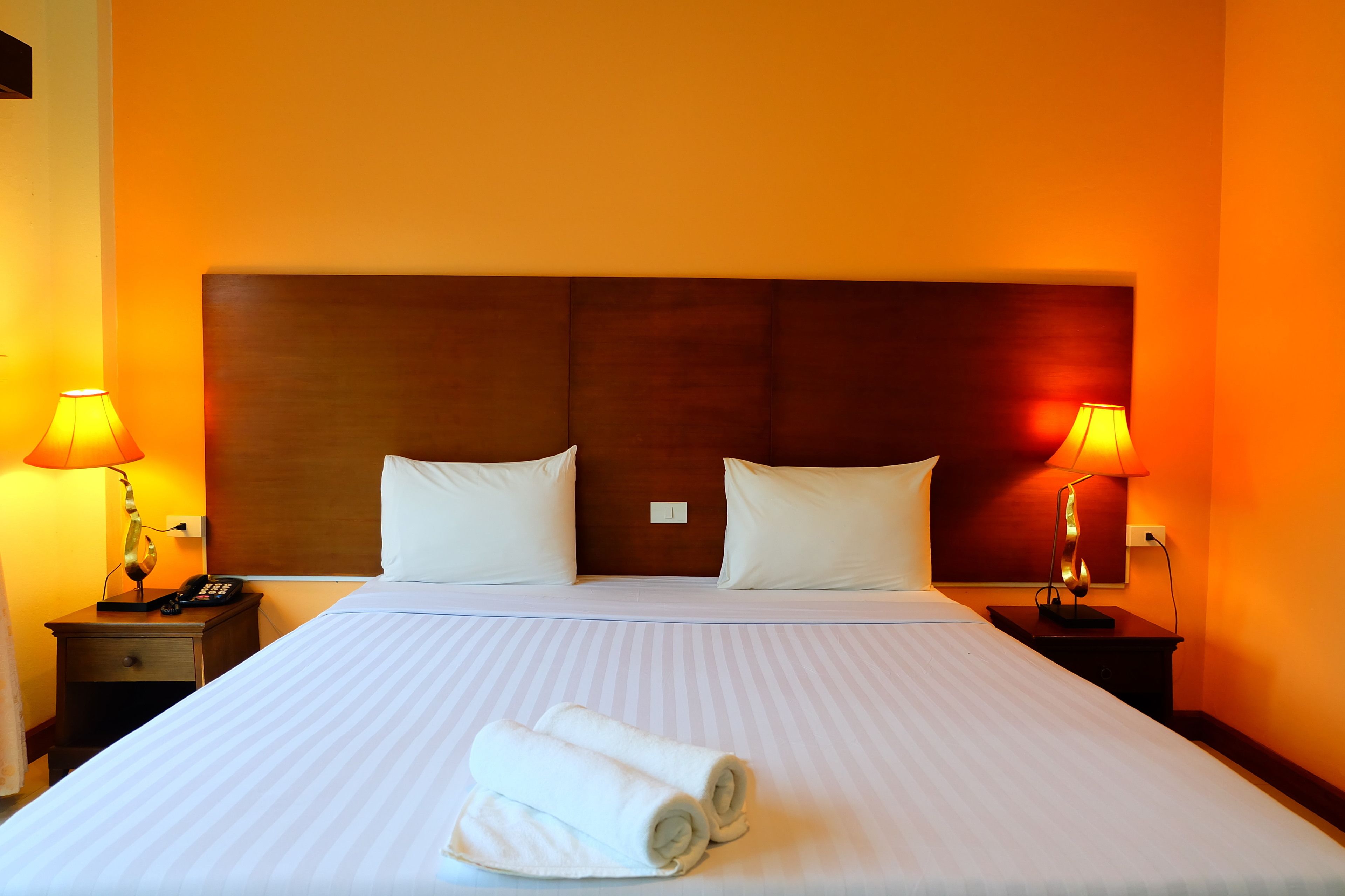 A hotel room with a large bed, two bedside lamps, and a neatly made bed with rolled towels.