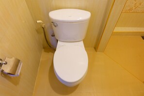 Un inodoro blanco en un baño con baldosas color beige y una zona de ducha.