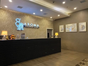 A reception desk with a neon sign for Aroma Wellness & Spa, framed artwork on the wall, and a plush rug. - Livingston Hotel (Sandakan)
