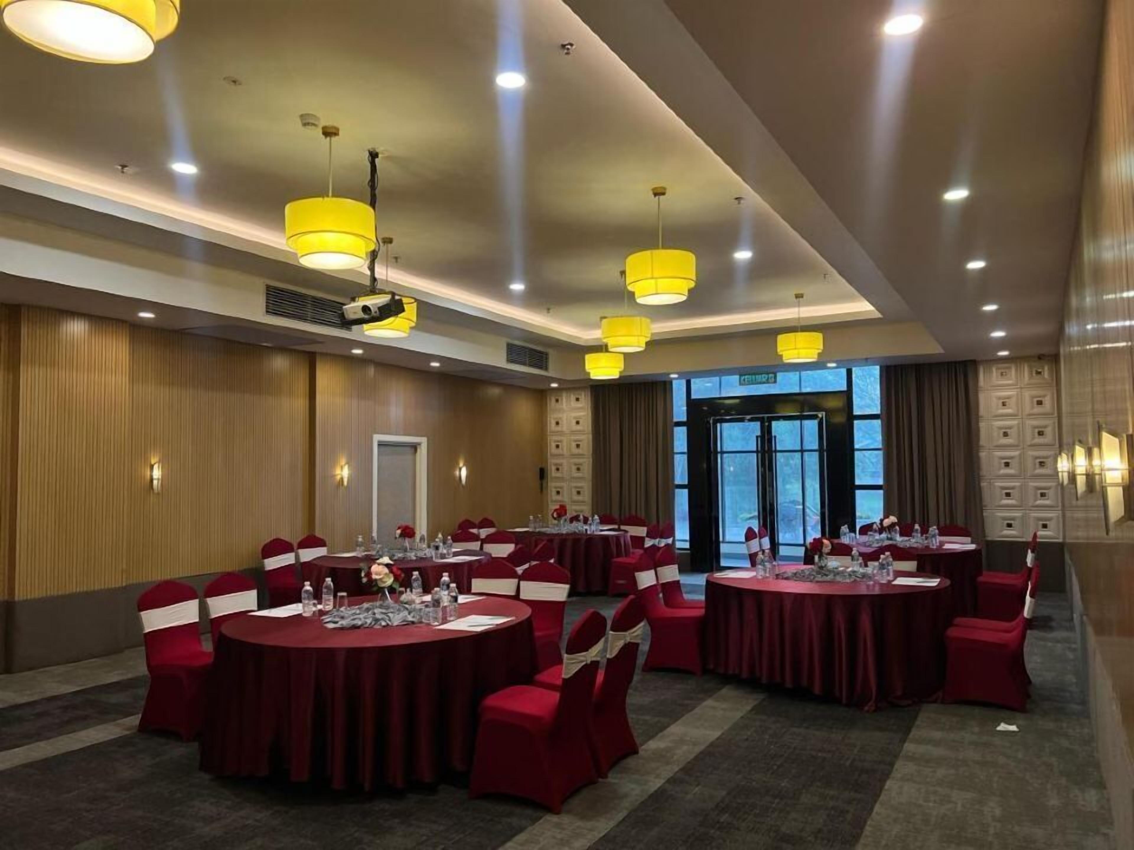 A conference room with multiple tables, red chairs, and yellow pendant lights.